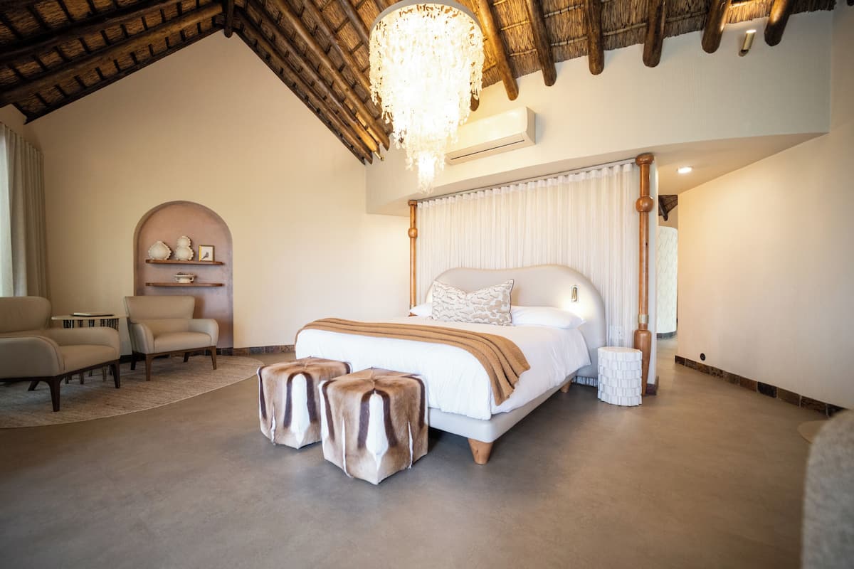 Une chambre avec un grand lit, un lustre, un plafond en bois et une petite table ronde.