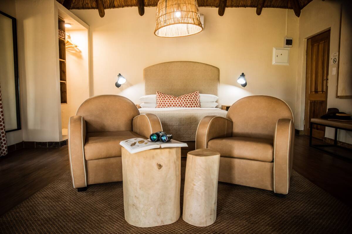 Une chambre à coucher avec un grand lit, deux fauteuils, une petite table et un luminaire suspendu.