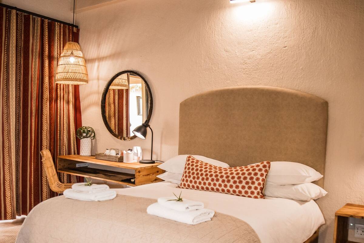 Un lit bien fait, avec une tête de lit en bois, une table de chevet avec une lampe et un miroir accroché au mur.