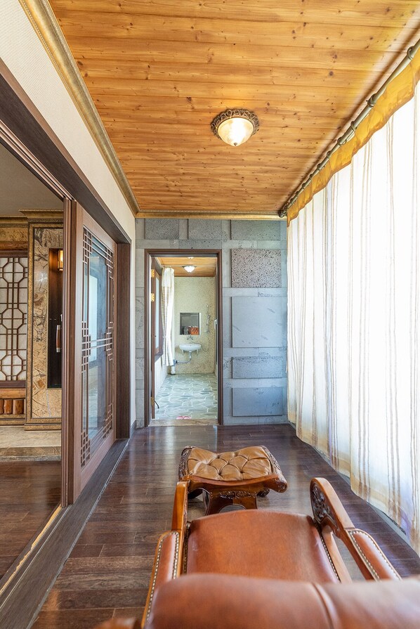 Un pasillo con piso de madera, un sillón de cuero y vista a un baño con lavamanos y espejo.