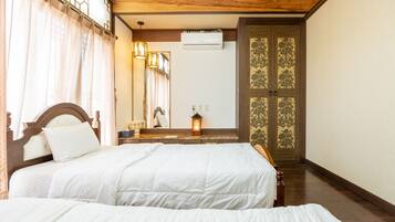 Habitación de hotel con dos camas, techo de madera, un espejo, unidad de aire acondicionado y una puerta tradicional con motivos florales.