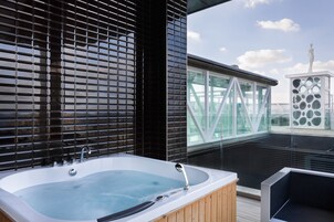 Un jacuzzi moderno al aire libre con terraza de madera, barandilla de vidrio y vistas del horizonte de la ciudad.