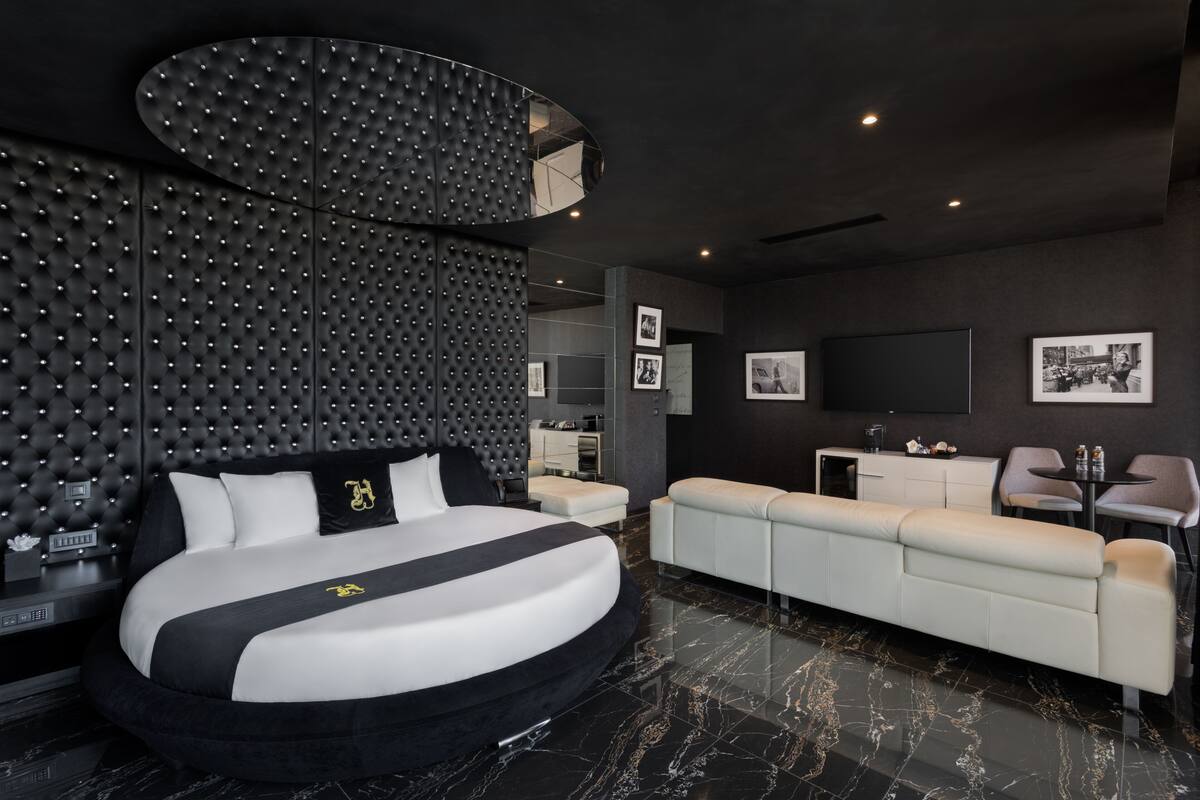 A modern bedroom with a large bed, a sofa, a TV, and a wall with a unique textured design.