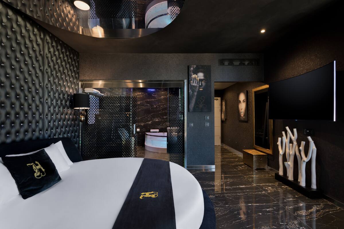 A modern hotel room with a large bed, a black and white color scheme, a round mirror, and a wall-mounted TV.
