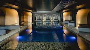 Ein modernes Spa mit einem zentralen Pool, Sitzbereichen und einer gemusterten Decke.