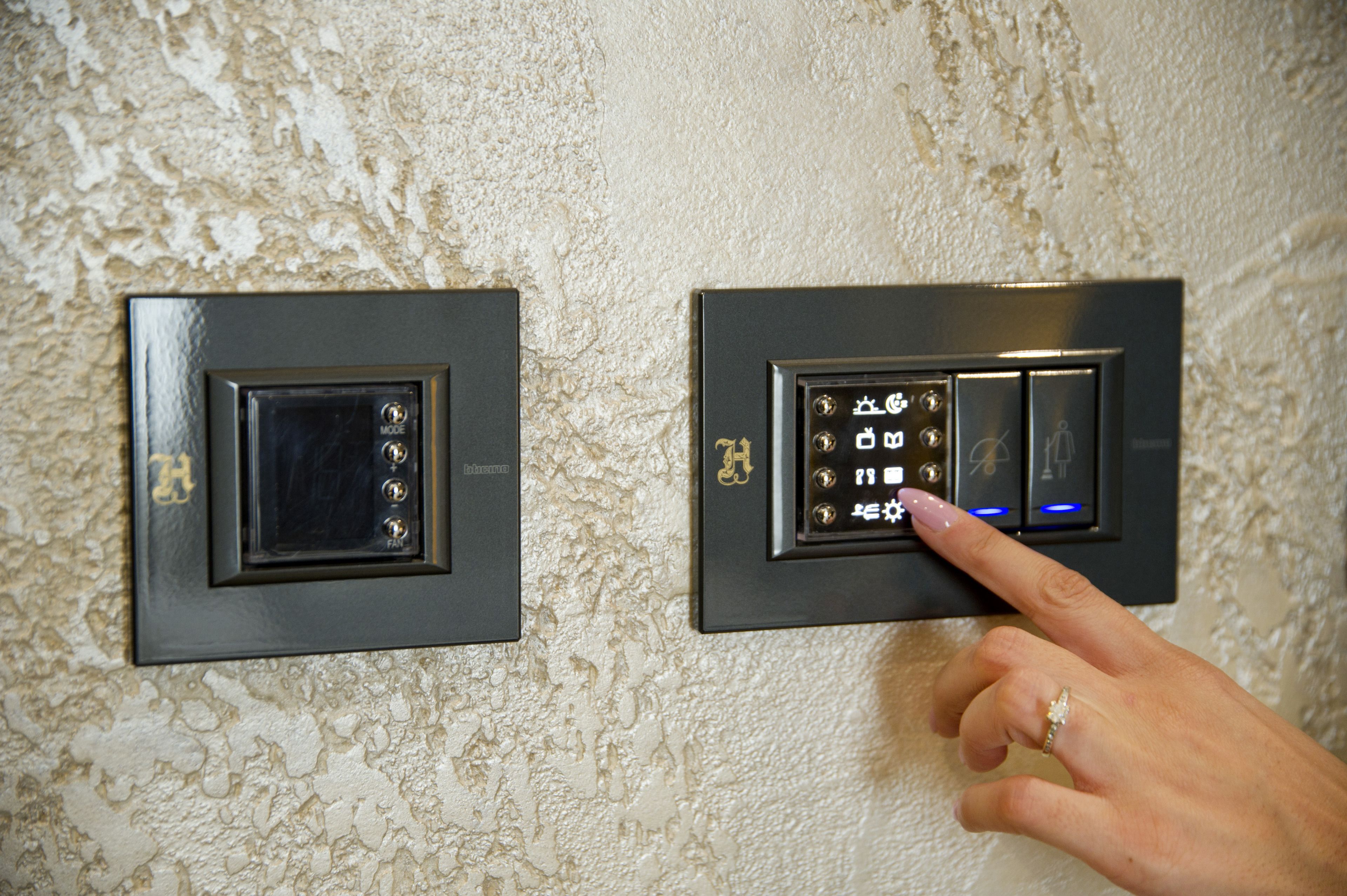 Un panneau de commande fixé au mur, doté d’un écran numérique et de boutons, et une main pointant vers un bouton.
