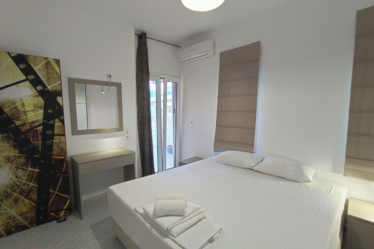 A hotel room with a large bed, a bedside table, a mirror, and a view of the outside through a sliding door.
