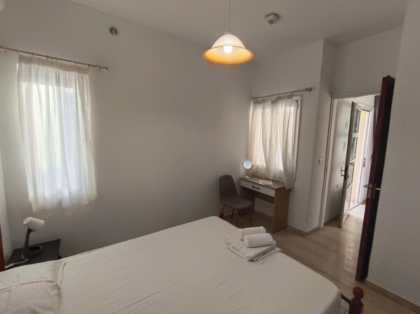 A bedroom with a bed, a desk with a chair, a mirror, and a hanging light fixture.