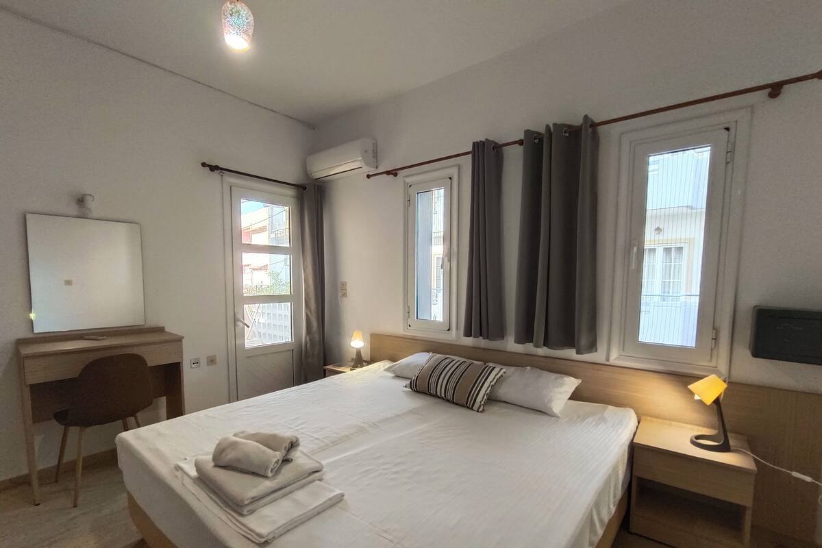 A hotel room with a bed, a desk, a chair, a lamp, and a TV.