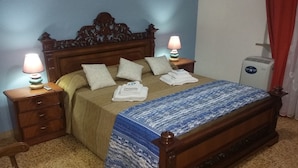 Una cama bien hecha con un edredón estampado, dos lámparas de noche y una mesita de noche con una lámpara.