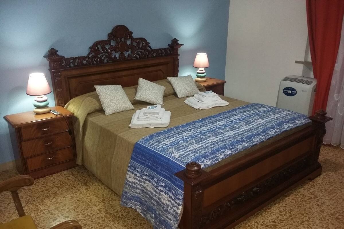 A neatly made bed with a patterned blanket, two bedside lamps, and a small bedside table with a lamp.
