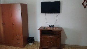 Habitación con armario de madera, televisor montado en la pared y una pequeña mesa de madera con un control remoto y un objeto decorativo encima.