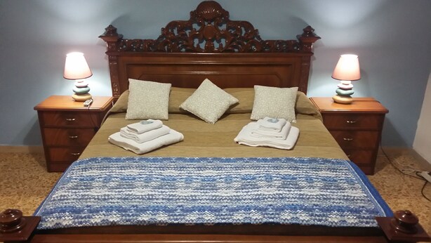 Una cama bien tendida con una manta de diseño azul y blanco, dos lámparas de noche y un cabecero de madera.