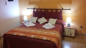 Una cama bien hecha con una colcha estampada, dos lámparas de noche y una mesita de noche con lámpara.