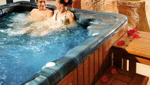 A hot tub with a wooden bench and flowers, surrounded by blue patterned walls and a tiled floor.
