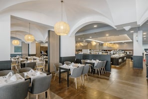 A spacious dining area with multiple tables and chairs, a central bar area, and a kitchen in the background.