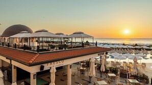 A rooftop bar with a pool, outdoor seating, and a view of the sunset over the ocean. - Alua Helios Bay (Nessebar)