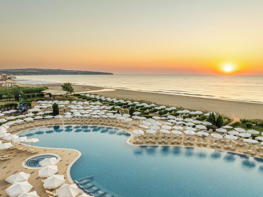 Een resort met zwembad, strand en uitzicht op de zonsondergang.