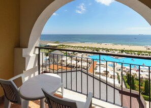 A balcony with a view of a beach, pool, and ocean.