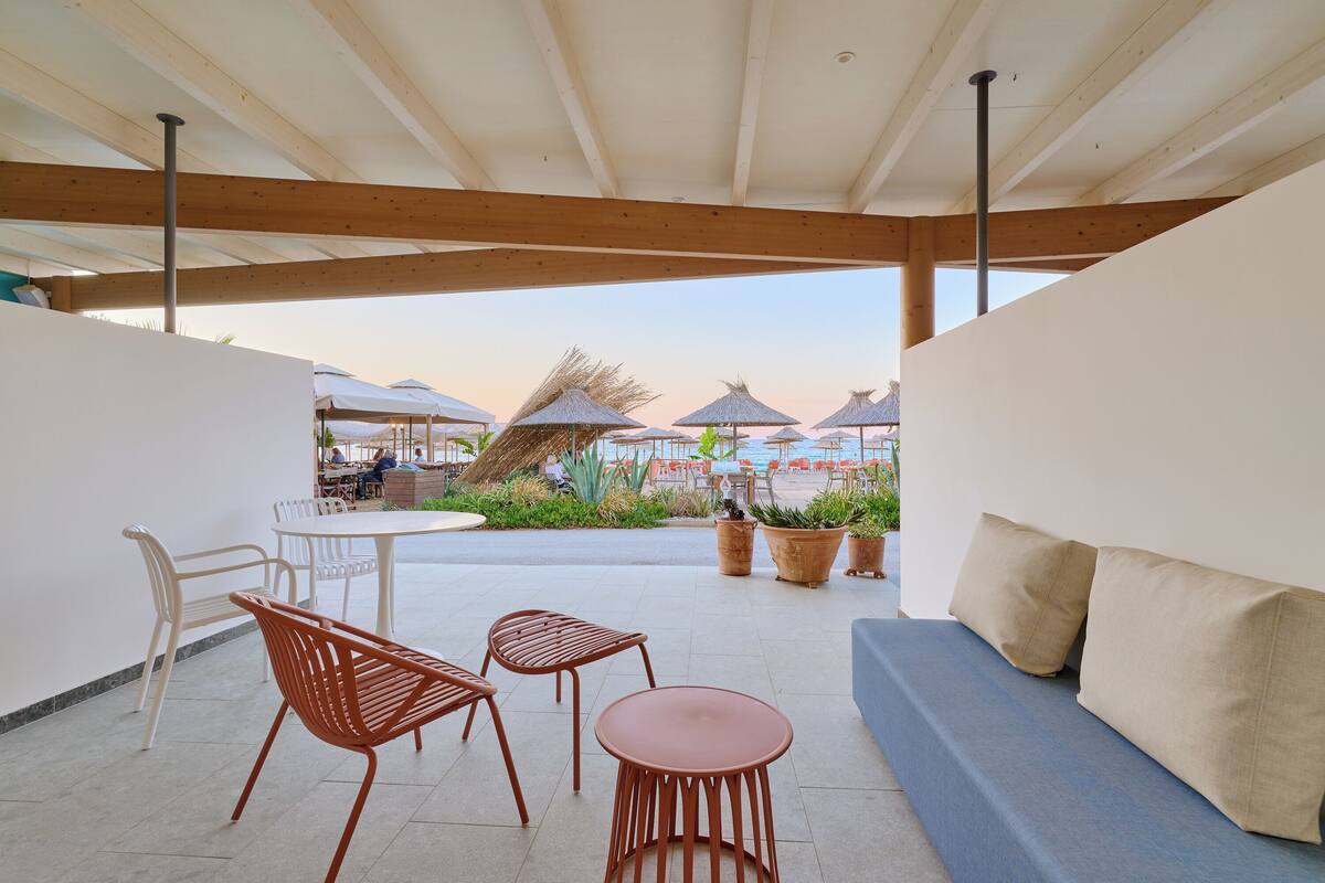 A covered outdoor seating area with a table and chairs, a sofa, and potted plants.