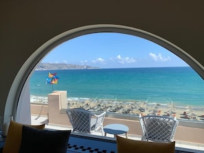 Een balkon met uitzicht op zee, witte rieten stoelen en een kleurrijke windmolen.