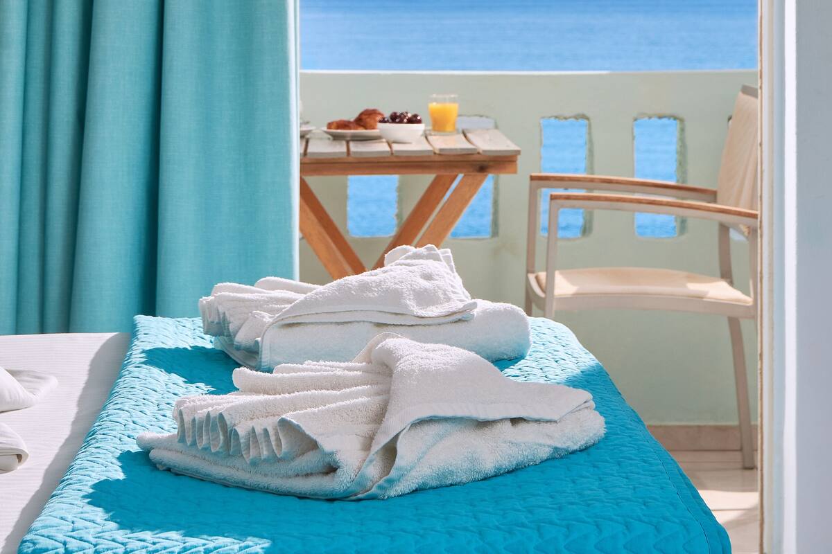 A room with a bed, a table with a chair, and a view of the sea.