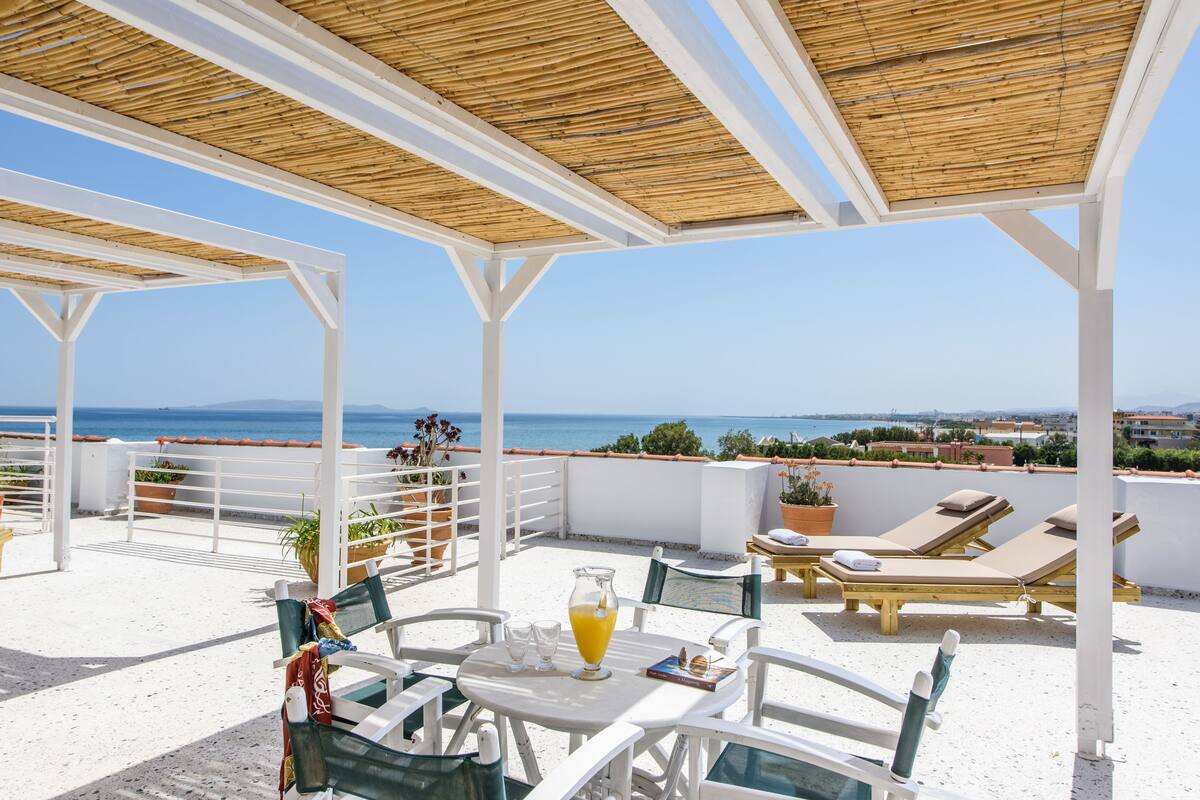 A covered outdoor seating area with tables and chairs, overlooking a scenic view of the sea.