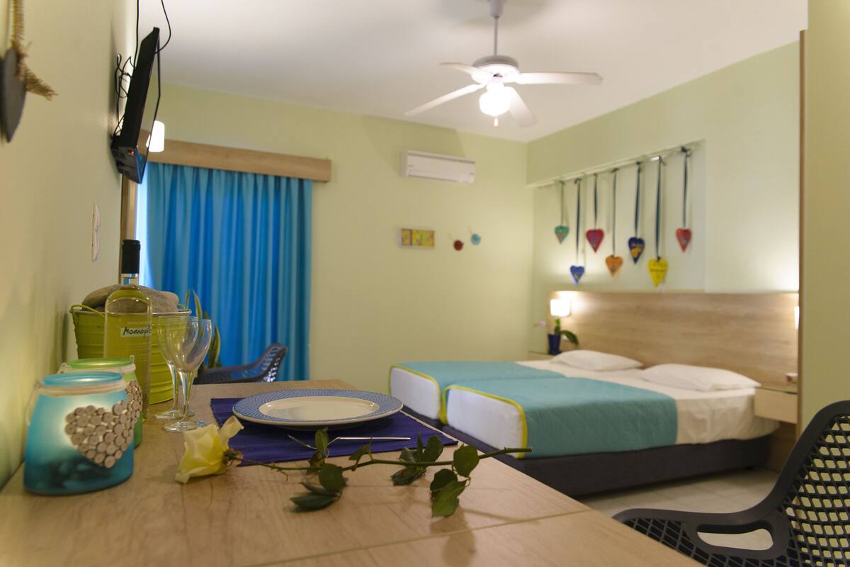 A hotel room with a bed, a table with a vase and a plate, a ceiling fan, and a window with curtains.