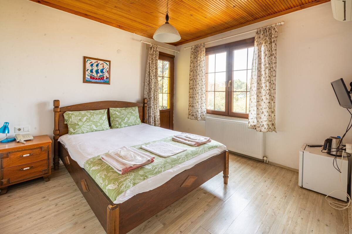 A bedroom with a wooden bed, a nightstand, a desk with a computer, and a window with curtains.