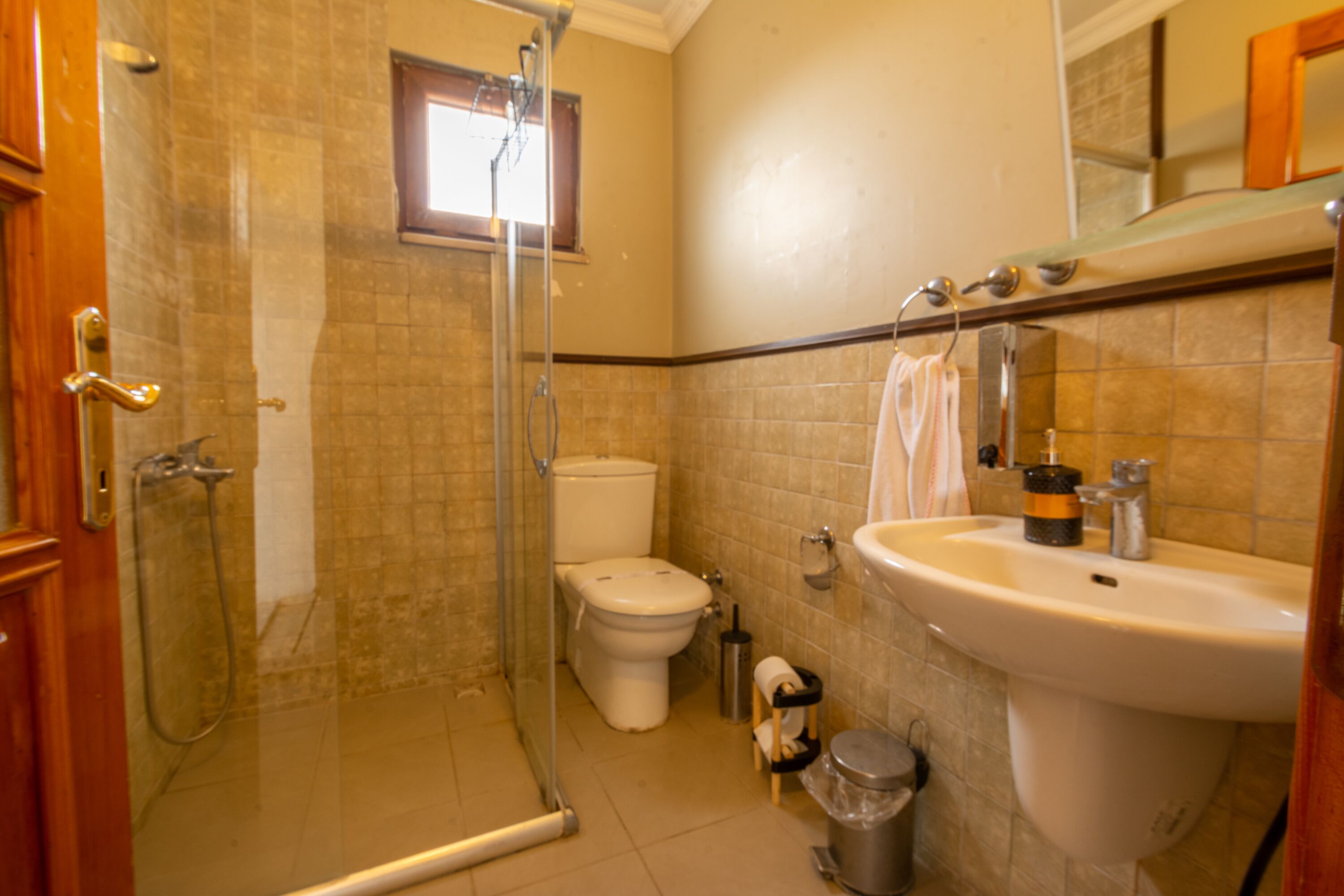 A bathroom with a glass shower enclosure, a toilet, a sink, and a trash can.