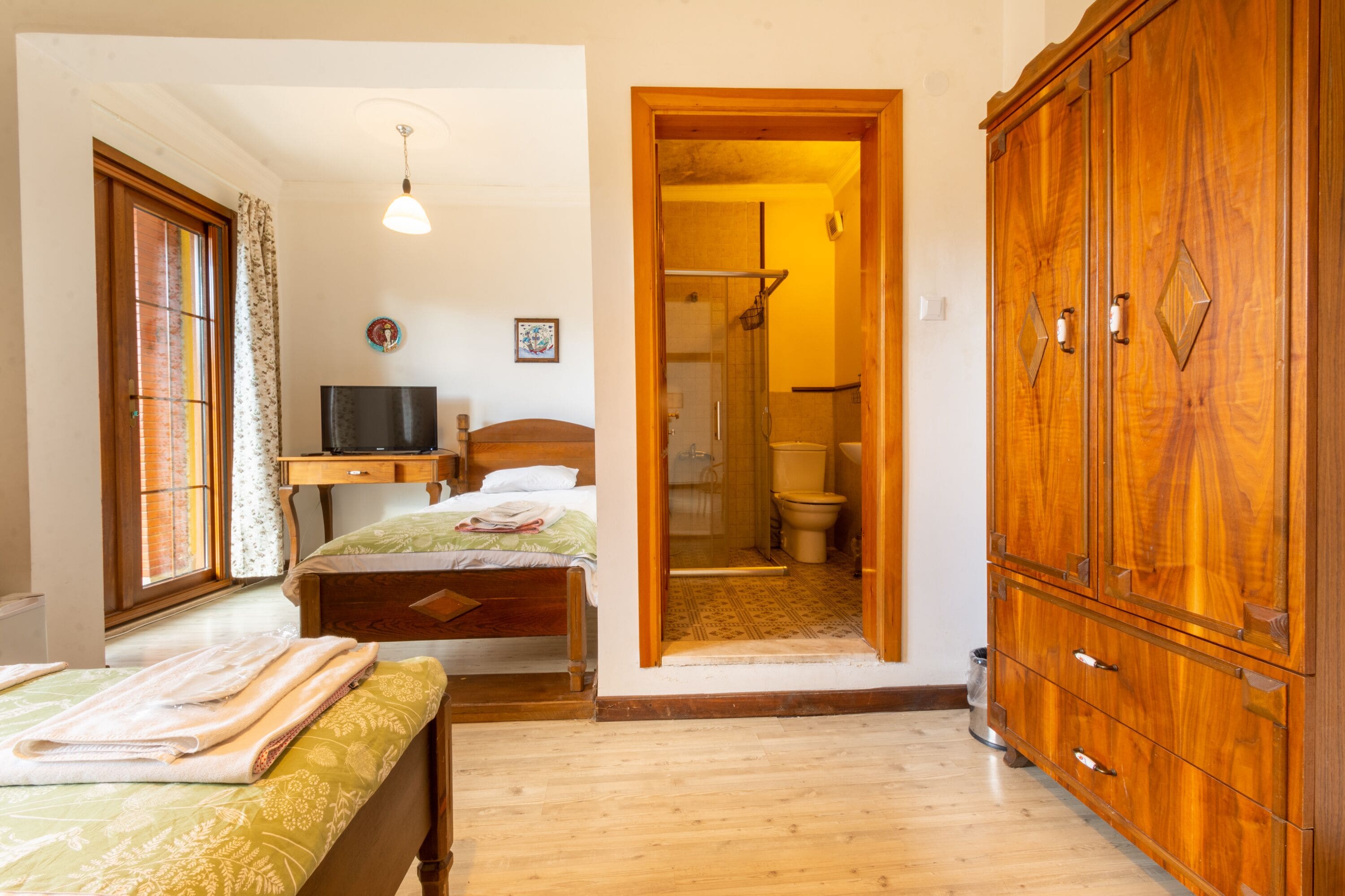 Un dormitorio con una cama de madera, televisor, armario y baño a la vista a través de una puerta abierta.