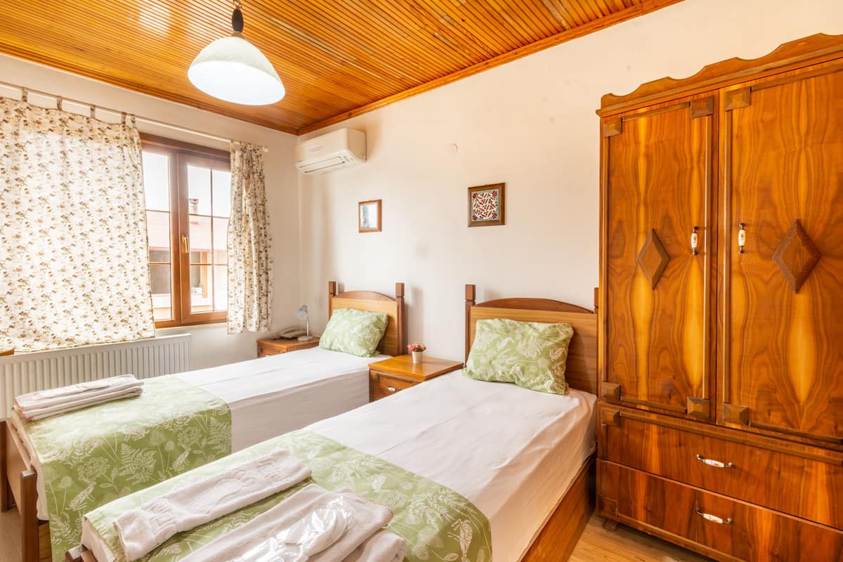 A double room with two beds, a wooden wardrobe, a window with curtains, and a ceiling light.