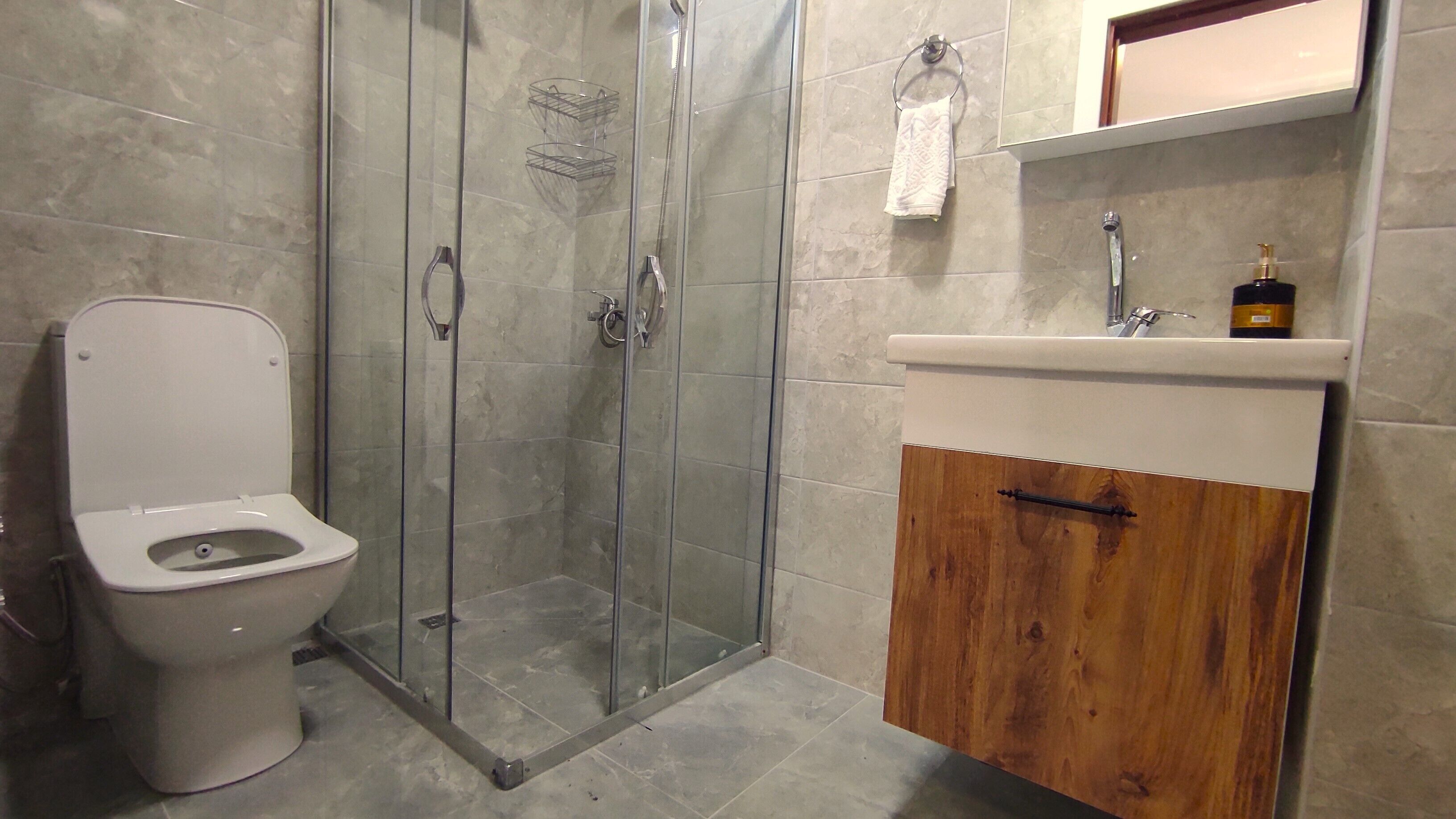 Un baño con inodoro, ducha envuelta en vidrio y tocador de madera con lavamanos.