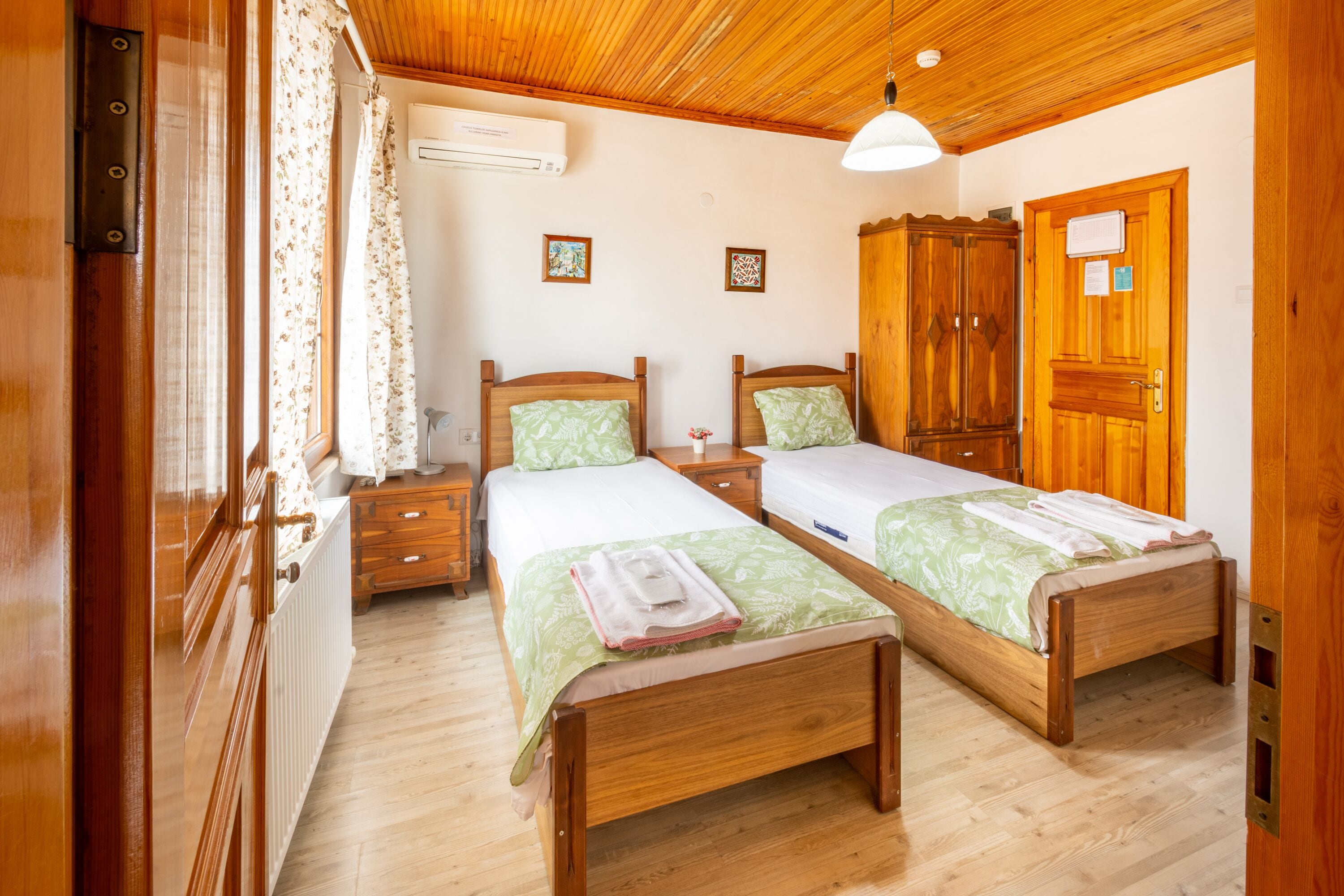 Une pièce avec deux lits en bois, une armoire en bois, un radiateur et une fenêtre avec des rideaux.