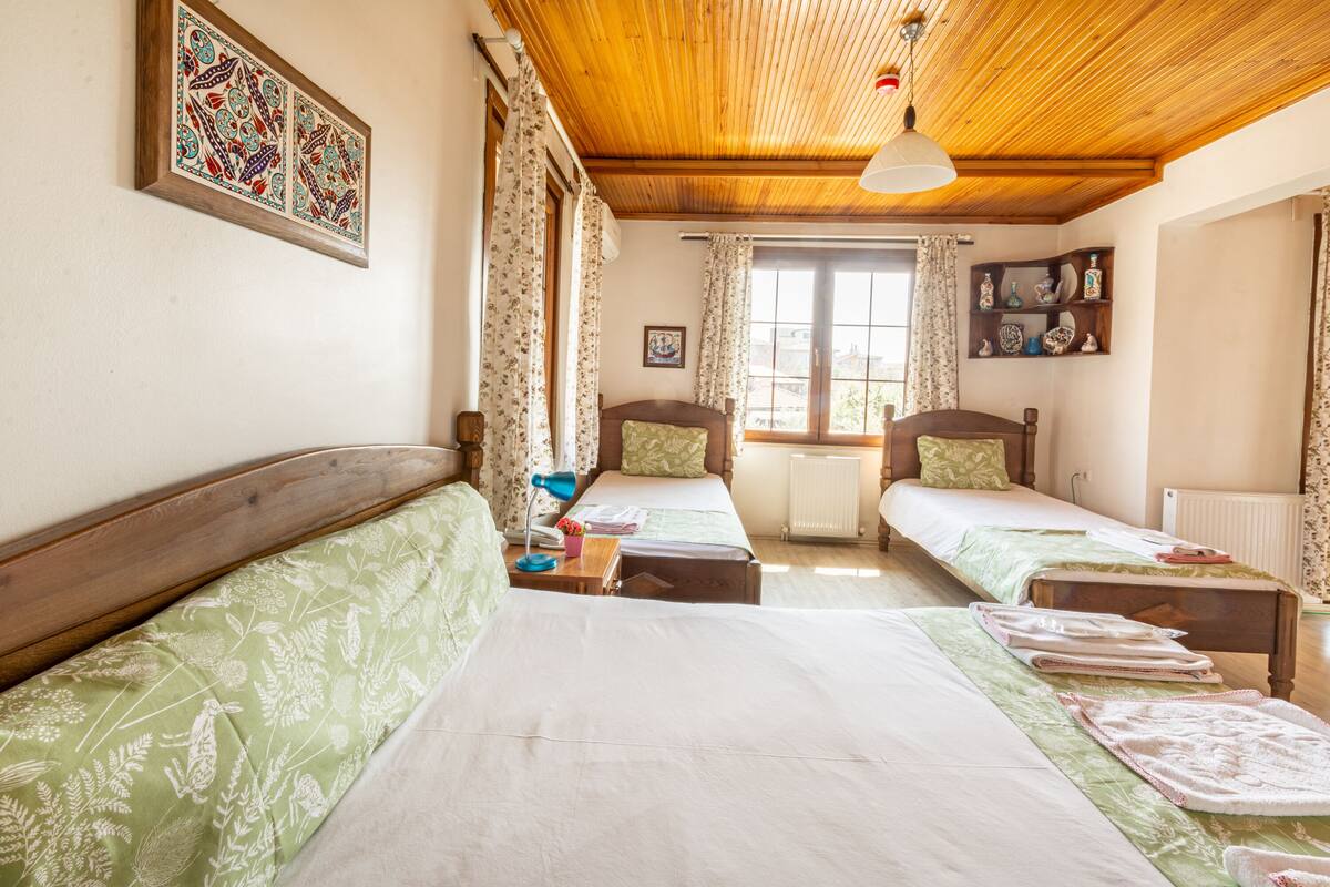 A room with two beds, a wooden ceiling, and a window with curtains.
