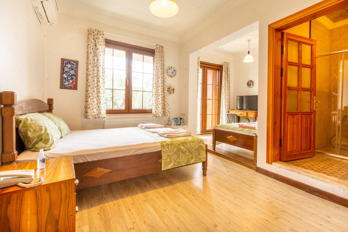 A spacious bedroom with a large bed, a wooden nightstand, a desk, and a television.