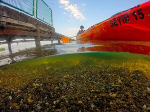 Un kayak rojo con el número 15, un puente y una costa rocosa.
