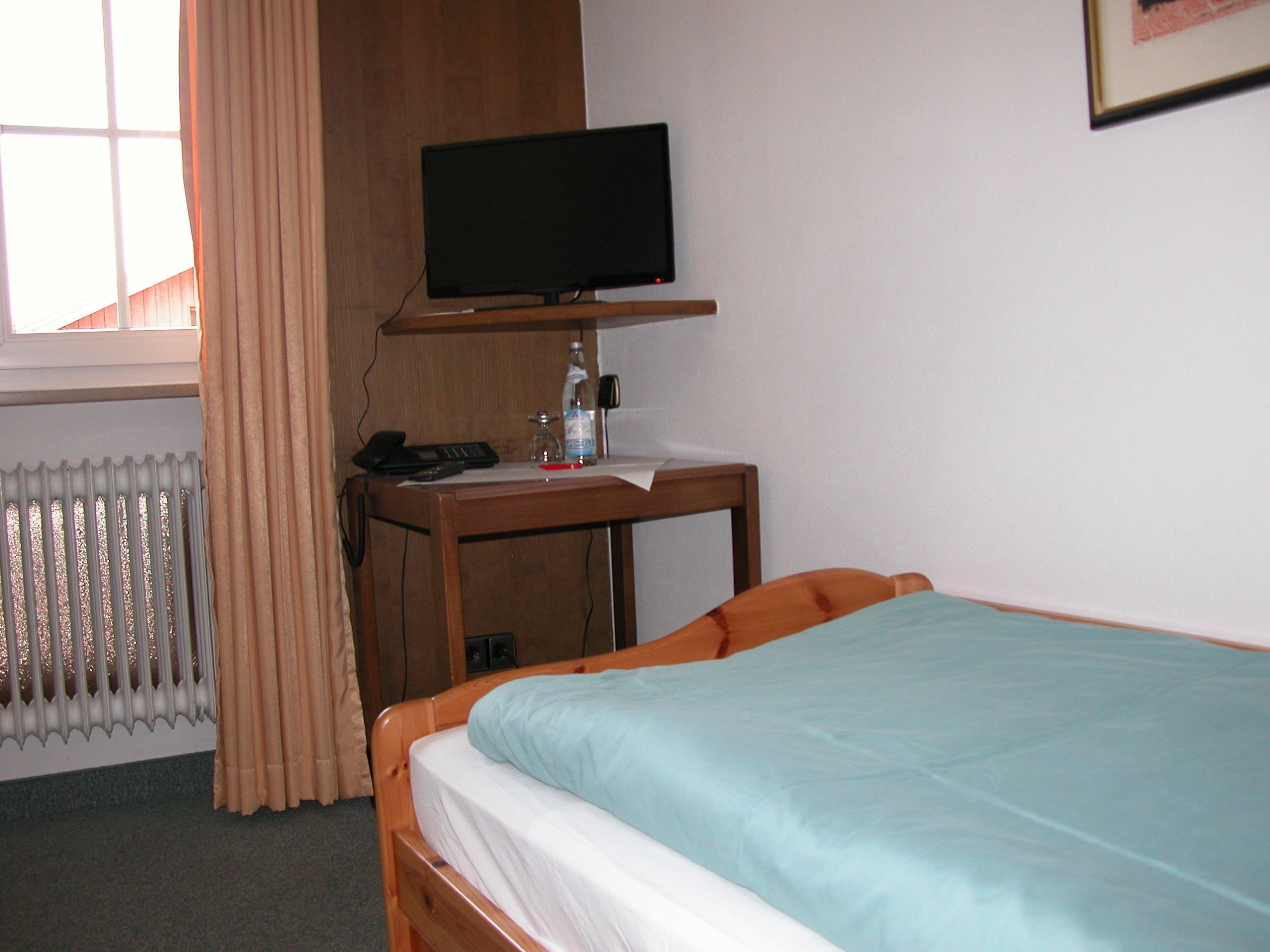 A hotel room with a bed, a desk with a television, a telephone, and a bottle of water.