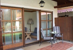 A patio with a table and two chairs, a lamp, and a view through a sliding glass door.