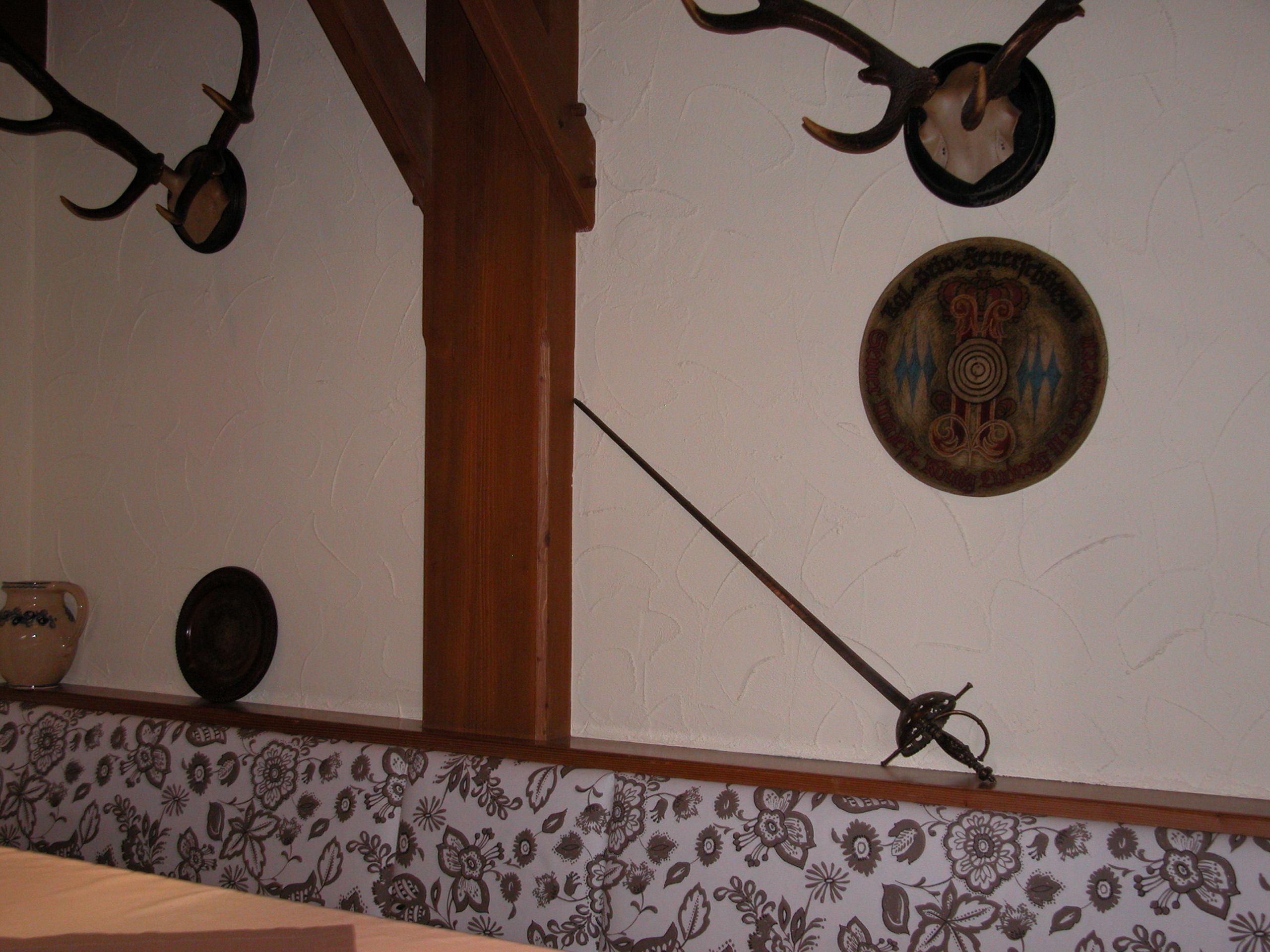 Een kamer met behang met een patroon, een houten balk en een decoratief bord aan de muur.