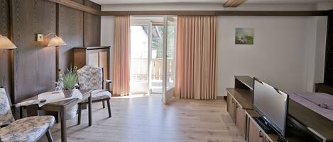 A spacious living area with a wooden floor, a television, and a dining table with chairs.