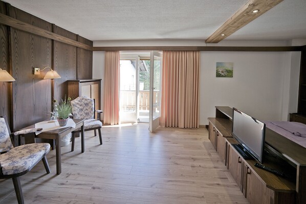 A spacious living area with a wooden floor, a television, and a dining table with chairs. - Hotel zum Hirschhaus (Ruhpolding)