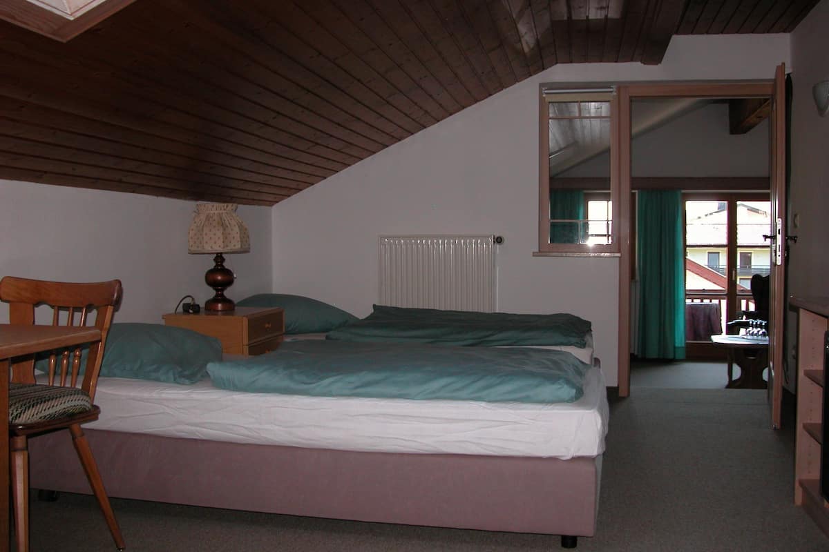 A bedroom with a bed, a chair, a nightstand, a lamp, a radiator, and a window with curtains.