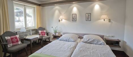 A hotel room with a double bed, two bedside tables, a chair, a desk, and a window with curtains.