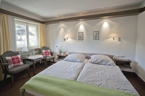 A hotel room with a double bed, two bedside tables, a chair, a desk, and a window with curtains.