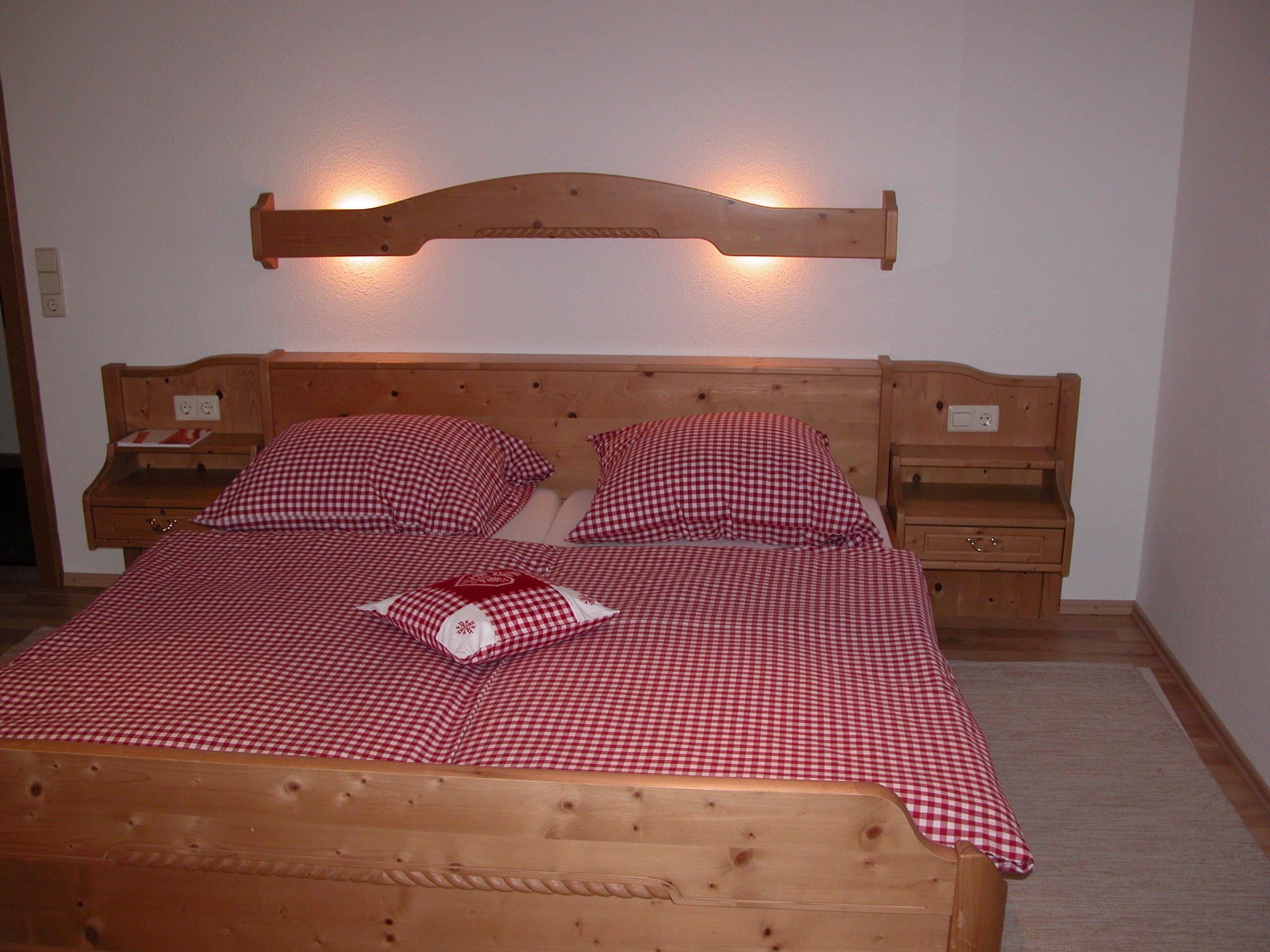 A wooden bed with a headboard, two bedside tables, and a red and white checkered bedspread.
