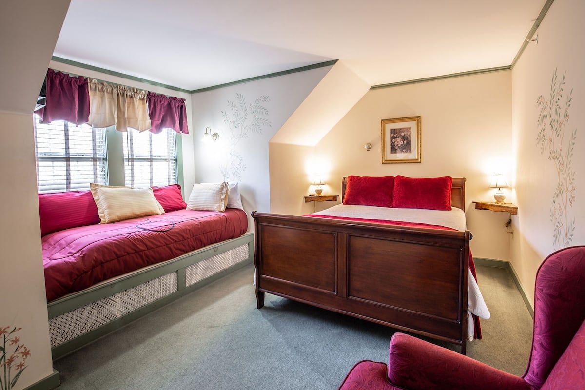 A bedroom with a bed, a chair, and a nightstand with a lamp.