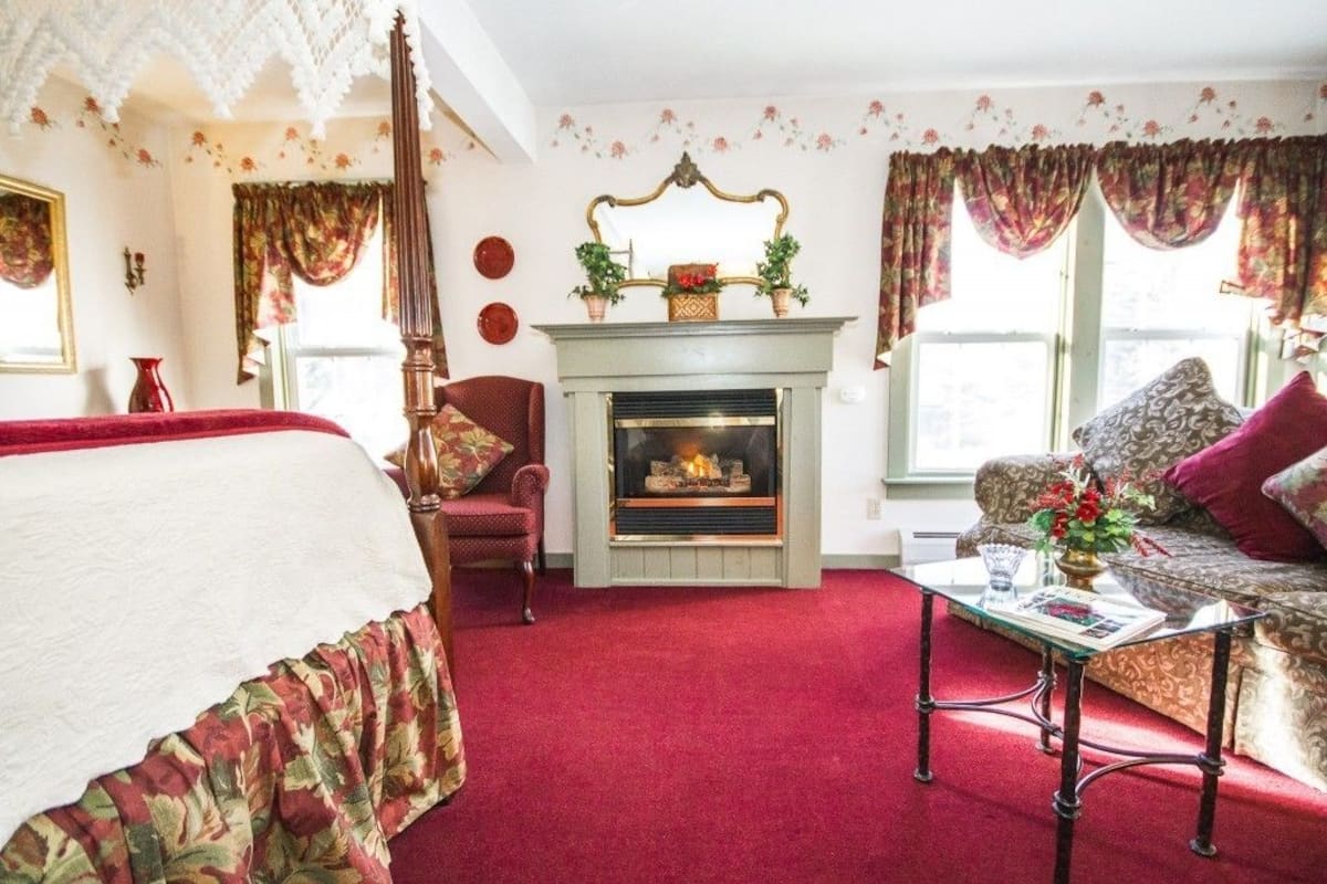 A room with a fireplace, a bed, a sofa, and a table with a vase of flowers.