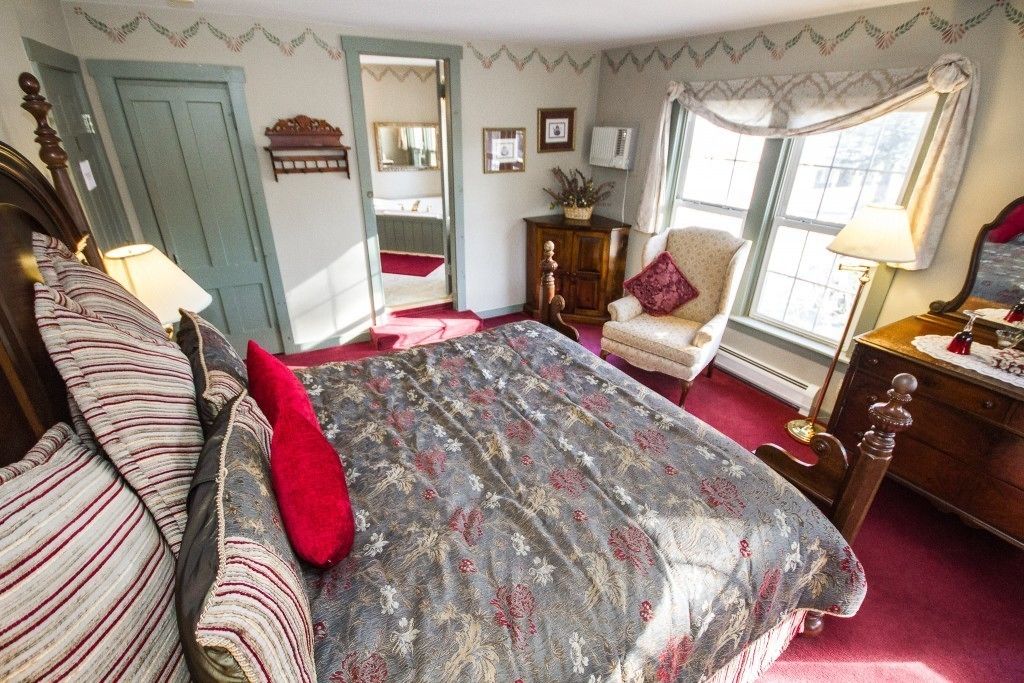 Un dormitorio con una cama grande, una silla, un aparador y una ventana con cortinas.