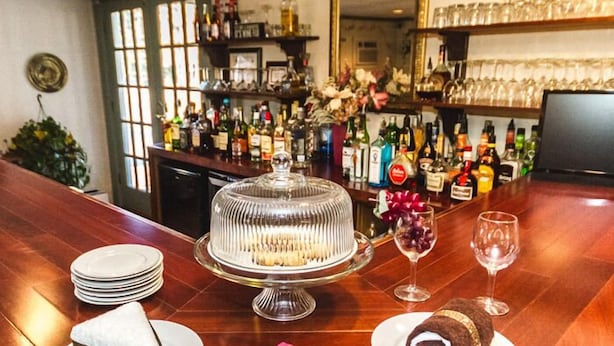 A bar area with a cake on a glass stand, plates, a pink napkin, and a rolled dessert on a plate. - Rosewood Country Inn (Bradford)